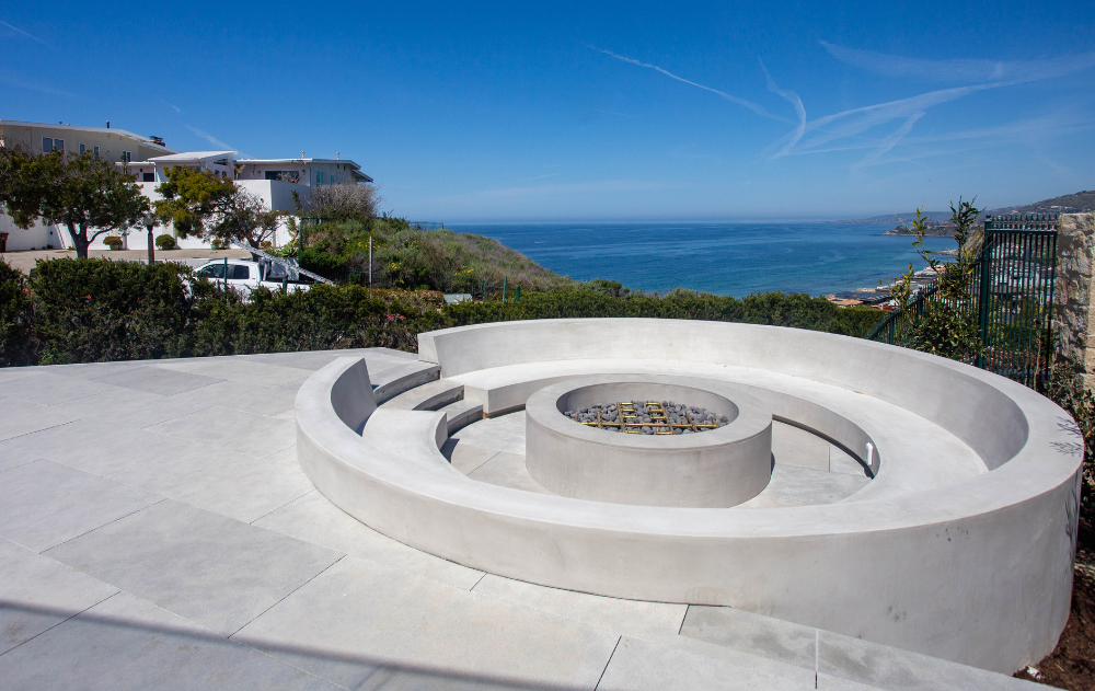 Luxury outdoor living space featuring natural stone hardscaping, a fire pit, and ocean views at an Orange County residence.