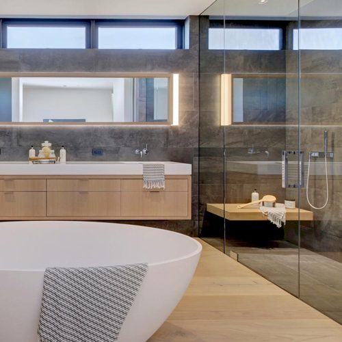 A modern bathroom featuring a freestanding bathtub, wooden vanity, large mirror with lighting, and a glass-enclosed shower area.