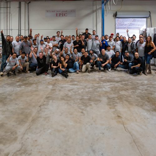 The EPIC family gathers in an industrial setting, smiling and raising hands, showcasing unity and enthusiasm in a group photo.
