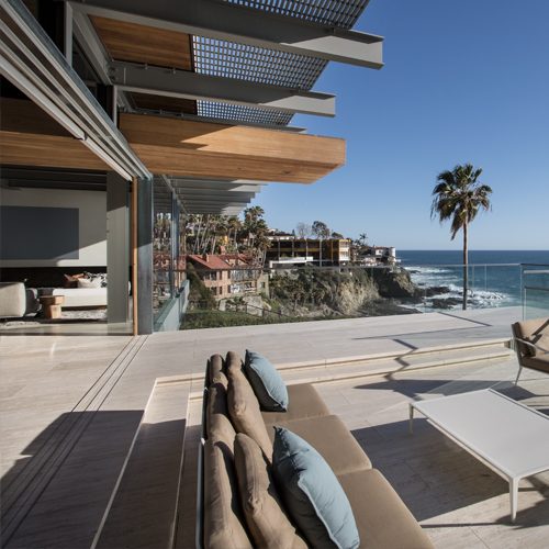 A luxurious beachfront patio with modern furniture, an outdoor seating area, glass railings, and a stunning ocean view.